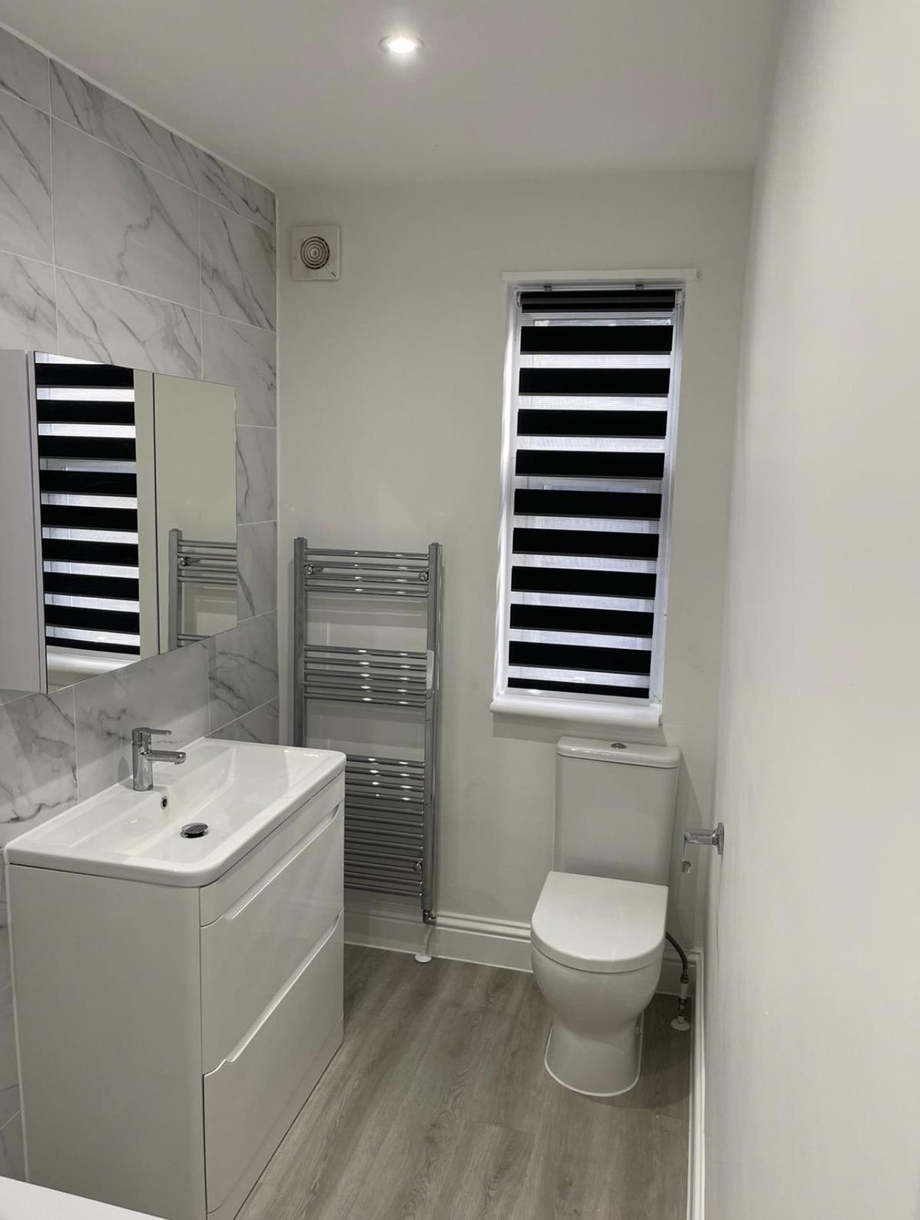Renovated bathroom with marble-effect tiling, vanity unit and chrome towel rail — bathroom decorating by MNC Construction, Essex