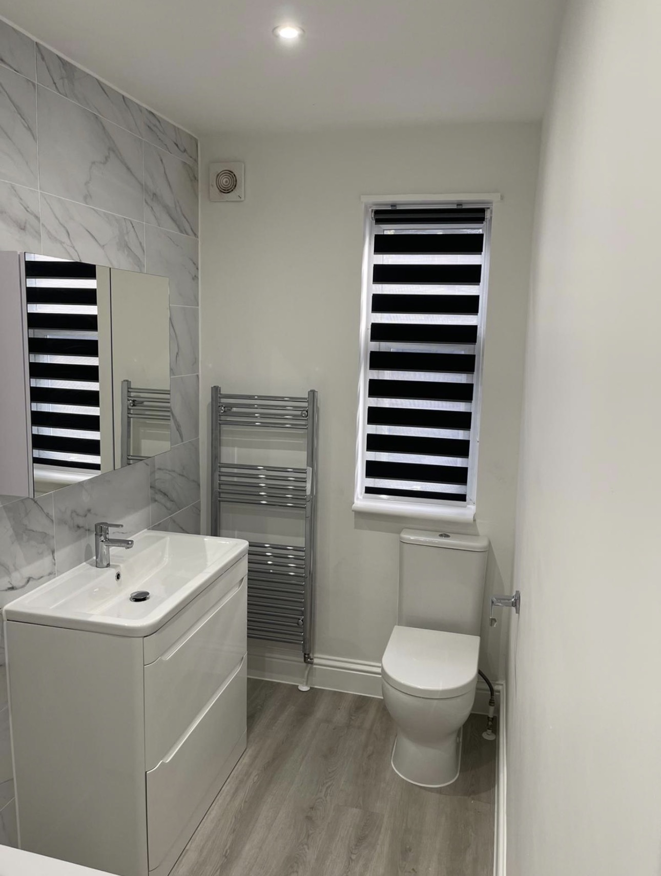 Renovated bathroom with marble-effect tiling, vanity unit and chrome towel rail — bathroom decorating by MNC Construction, Essex